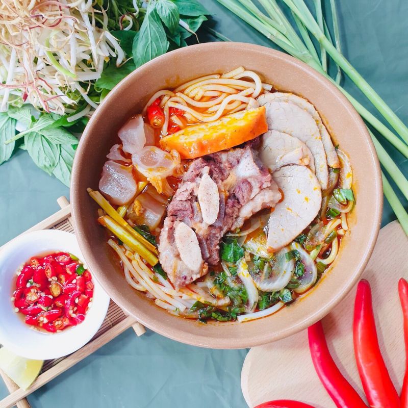Tô bún bò Huế đầy đủ với giò heo, chả, thịt bò và rau sống tươi xanh tại quán Bún Bò Kim Hương, Quận 1 – nổi bật với nước dùng ninh xương và mắm ruốc chuẩn Huế.