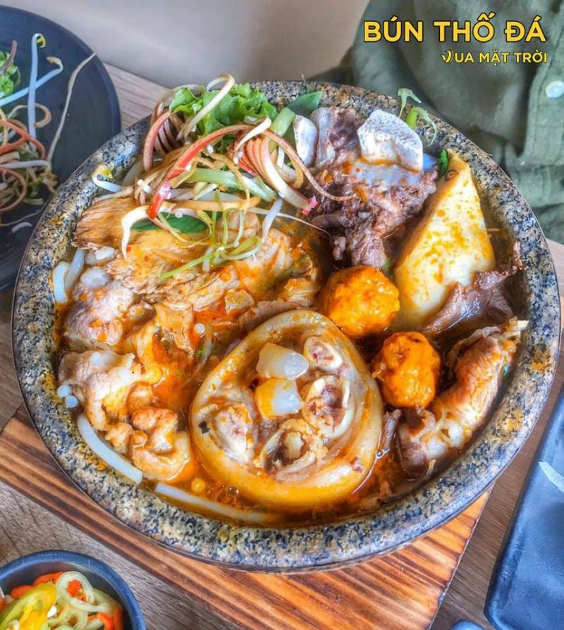 Tô bún bò Huế thố đá tại Vua Mặt Trời với thịt bò cắt dày, chả cua, gân bò và rau sống, bày biện trong thố đá giữ nhiệt – hấp dẫn và đậm vị.