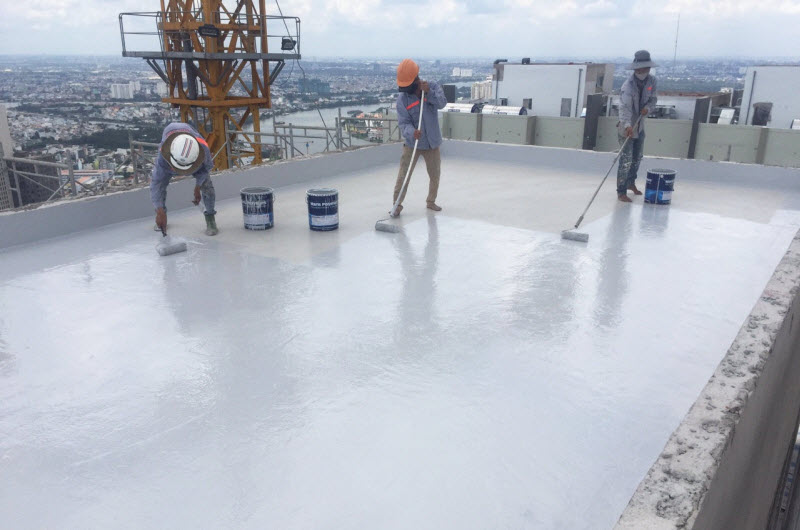 Ba công nhân đang thi công lớp sơn chống thấm màu trắng trên sân thượng tòa nhà, thuộc công ty Thuận Phát Như Ý, với các thùng sơn và dụng cụ chuyên dụng.