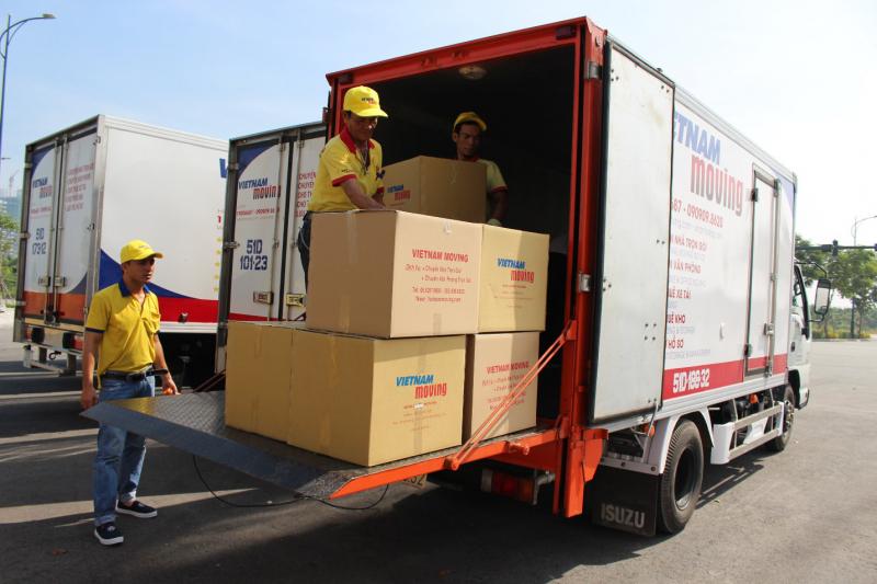 “Hai công nhân Vietnam Moving áo vàng đội mũ lưỡi trai đang bốc xếp sáu thùng carton in logo ‘Vietnam Moving’ bằng thang nâng đuôi xe tải, minh họa dịch vụ vận chuyển & relocation đạt ISO 9001:2015.”