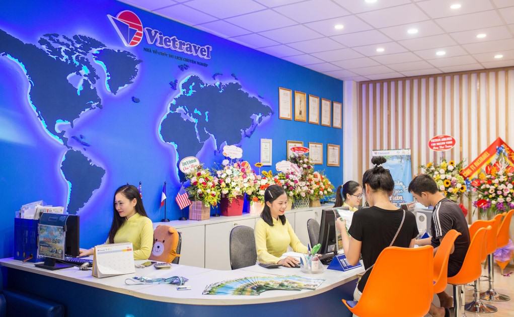 Nhân viên công ty du lịch Vietravel đang tư vấn tour du lịch cho khách hàng tại văn phòng hiện đại, nổi bật với bản đồ thế giới trên tường và không gian trang trí chuyên nghiệp.