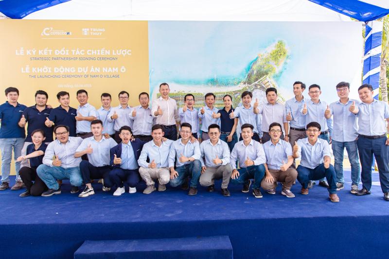 “Khoảng 25 nhân viên Solution Group mặc sơ-mi xanh nhạt đứng thành ba hàng trên sân khấu, giơ ngón cái trước backdrop lễ ký kết đối tác chiến lược và khởi động dự án Nam Ô Village, cho thấy tinh thần đồng đội trong dịch vụ tổ chức hội thảo trọn gói.”
