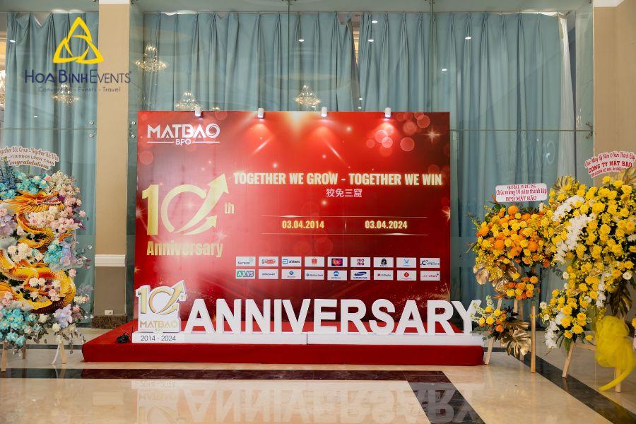 Sân khấu lễ kỷ niệm 10 năm thành lập công ty MATBAO với backdrop đỏ, biểu tượng 10th anniversary và hoa chúc mừng hai bên, do HoaBinh Events tổ chức.