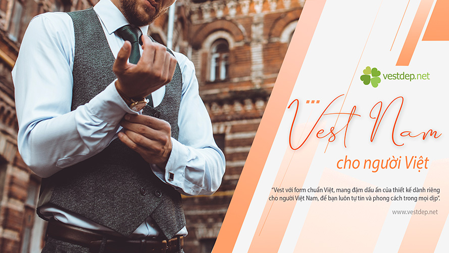 Người đàn ông mặc vest xám tinh tế, chỉnh tay áo trước tòa nhà cổ kính – hình ảnh đại diện cho chất lượng và phong cách tại cửa hàng bán áo vest Vestdep.net.