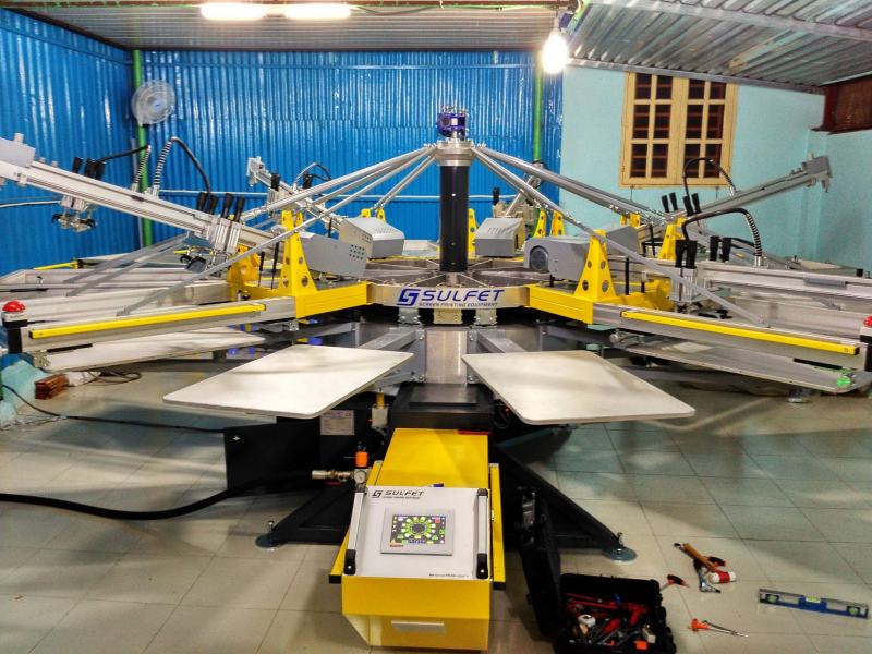 Máy in lụa đa trạm SULFET màu vàng – xám, bố cục hình bát giác trong xưởng may TP.HCM.