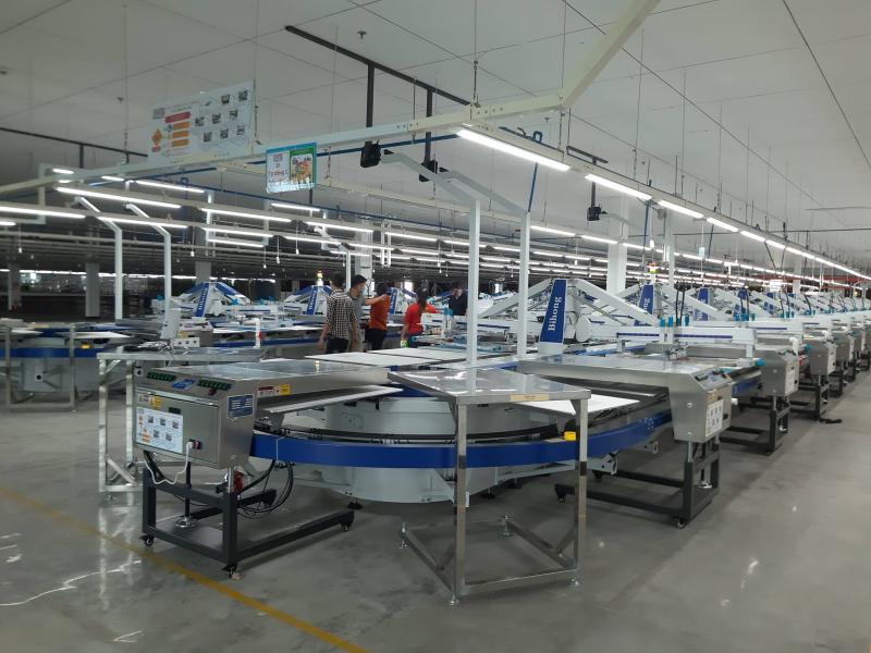Dãy máy in chuyển nhiệt tự động màu xanh – bạc xếp thành hàng dài trong nhà máy may hiện đại.