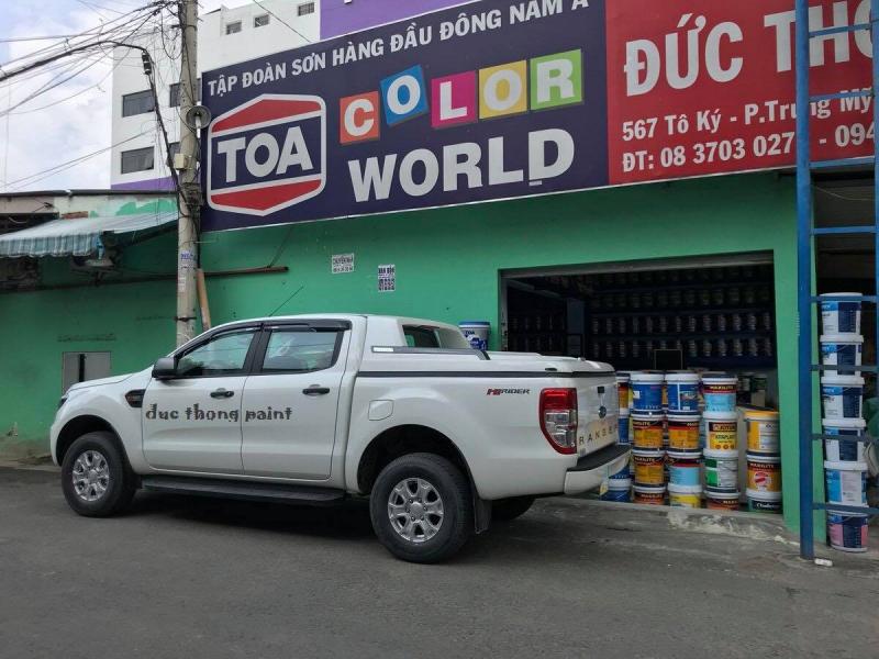 “Xe bán tải trắng in chữ ‘duc thong paint’ đậu trước cửa hàng TOA Color World (567 Tô Ký); trước và trong cửa hàng xếp chồng thùng sơn nhiều thương hiệu, minh họa đại lý Kim Loan Paint đa dạng 2 000 mã màu.”