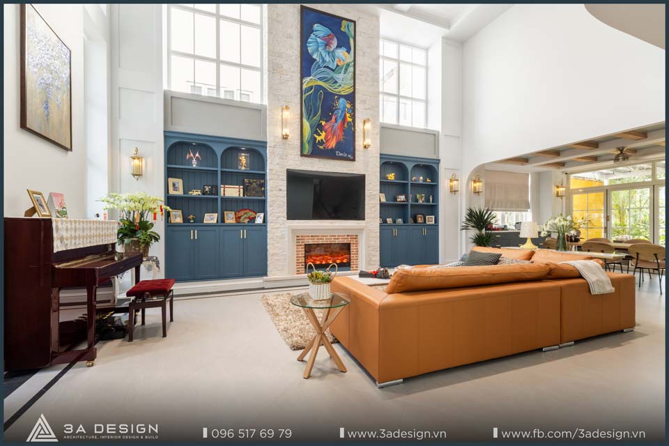Phòng khách biệt thự phong cách Địa Trung Hải với sofa da, tủ âm tường xanh, tranh treo nghệ thuật và lò sưởi – thiết kế bởi công ty nội thất 3A Design.