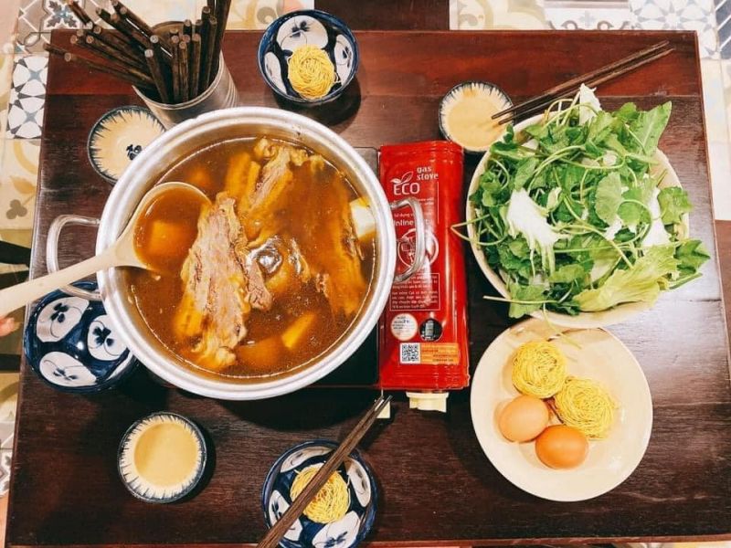 Nồi lẩu bò tại quán Nhà Gỗ với nước dùng hầm xương và thảo mộc, đầy đủ bò viên, gân, lá sách, phục vụ trong không gian thuần Việt.