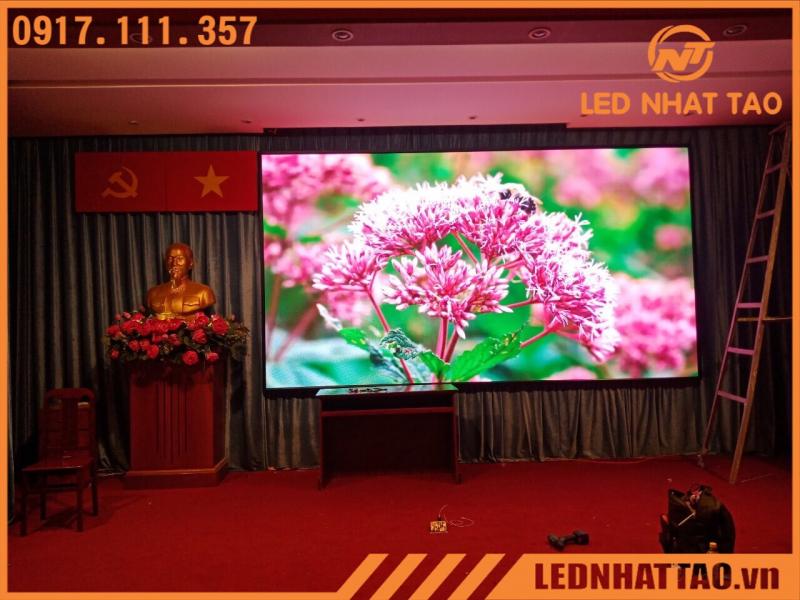 “Hội trường có bục tượng đồng, biểu tượng búa-liềm và ngôi sao vàng; giữa sân khấu là màn hình LED Nhật Tảo viền mỏng hiển thị cụm hoa hồng dại màu hồng rực, mô tả giải pháp lắp đặt màn hình LED tiết kiệm điện cho không gian sang trọng.”