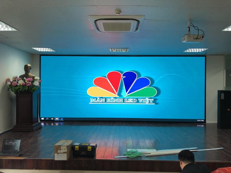 “Sân khấu hội nghị với sàn gỗ, màn hình LED siêu rộng hiển thị logo ‘Màn Hình LED Việt’; tượng đồng trang trí bên trái, trần treo máy chiếu và kỹ thuật viên D&Q đang lắp đặt, minh họa gói AV-Integration hoàn chỉnh.”