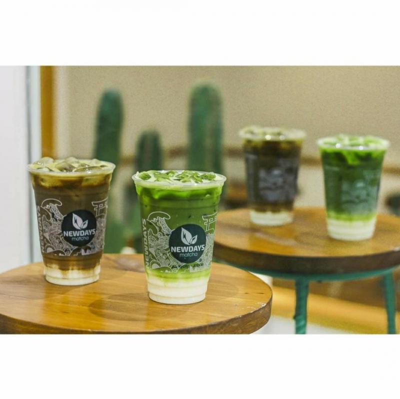 Ba ly matcha ngon Newdays đặt trên bàn gỗ, nổi bật với lớp màu xanh đặc trưng kết hợp sữa tươi.