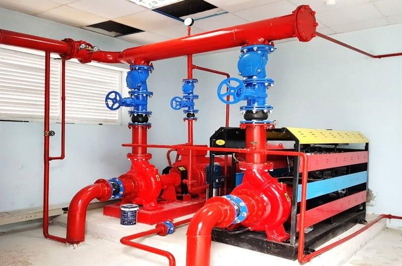 Hai bơm chữa cháy màu đỏ nối đường ống lớn, trên có van xanh; cạnh đó là động cơ diesel bọc khung, đặt trong phòng kỹ thuật PCCC.
