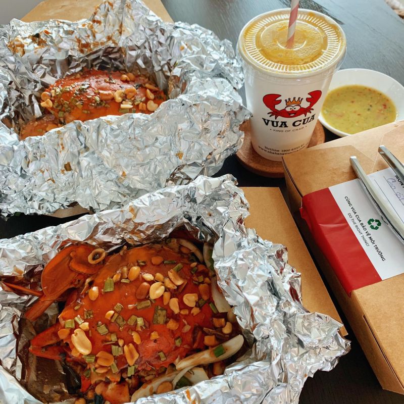 Hộp cua sốt Singapore và thức uống tại Vua Cua, đóng gói bằng giấy và bạc giữ nhiệt, kèm nước chấm và dụng cụ ăn – thể hiện sự chỉn chu và chất lượng trong từng phần ăn.