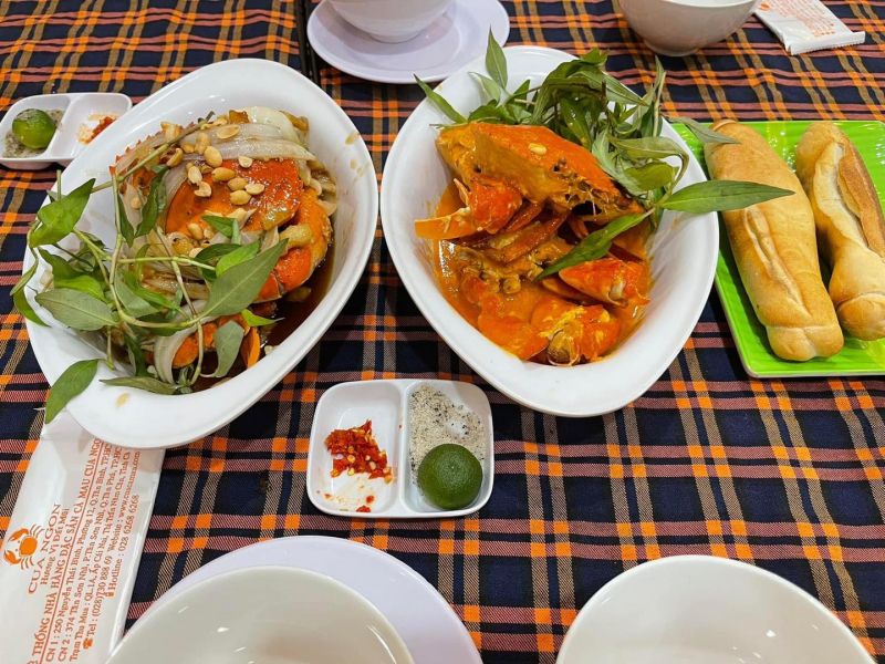 Hai dĩa cua sốt đậm đà, bày trên khăn bàn ca-rô cùng bánh mì, chanh, muối tiêu – đặc sản tại quán Ẩm Thực Sáu Cua, nơi hội tụ hương vị dân dã và giá cả bình dân.