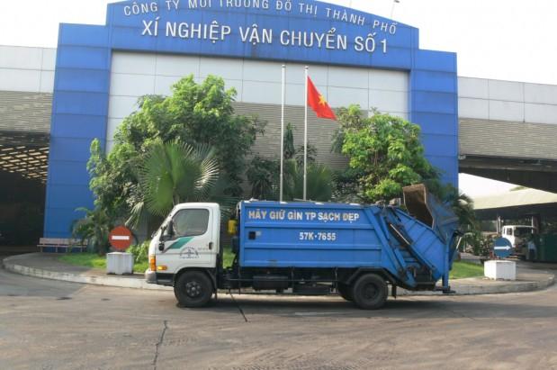 Xe rác màu xanh của Xí Nghiệp Vận Chuyển Số 1 TP.HCM đậu trước trụ sở với khẩu hiệu giữ gìn thành phố sạch đẹp.