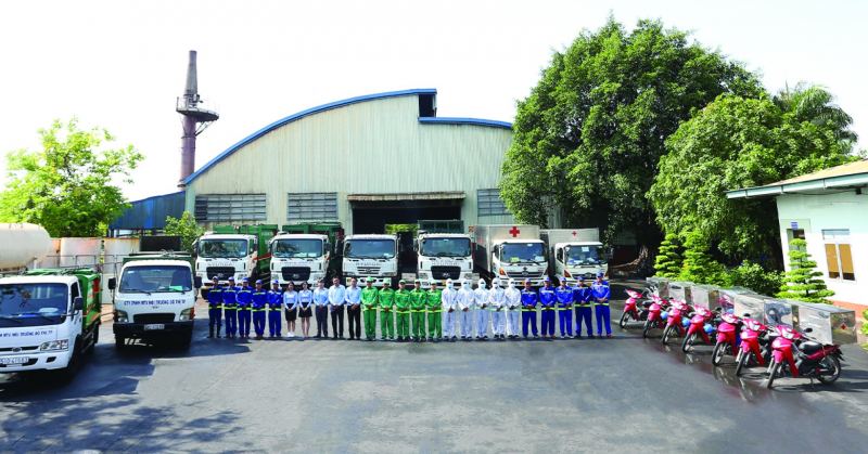 Nhân viên môi trường TP.HCM đứng hàng ngang trước dàn xe chuyên dụng và trụ sở nhà xưởng, thể hiện quy mô tổ chức và năng lực xử lý vệ sinh công nghiệp.