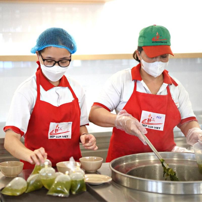 Hình ảnh nhân viên Bếp Lửa Việt đang chuẩn bị suất ăn học đường trong khu bếp công nghiệp hiện đại, thể hiện chất lượng dịch vụ cung cấp suất ăn trường học đạt chuẩn.

