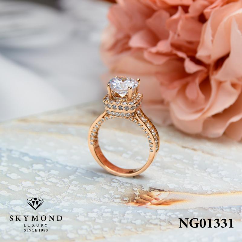 Nhẫn kim cương thương hiệu trang sức  Skymond Luxury mã NG01331 với viên chủ lớn dạng cushion cut, bao quanh bởi hàng trăm viên kim cương tấm, đặt trên nền vàng hồng sang trọng, nổi bật bên cạnh hoa hồng pastel.