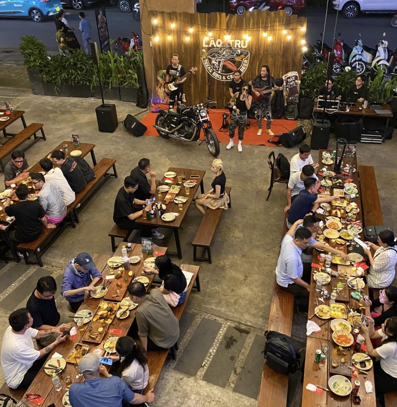 Tiệc BBQ ngoài trời tại quán Lão Trư với thực khách ngồi ăn uống và ban nhạc biểu diễn trực tiếp trên sân khấu nhỏ.