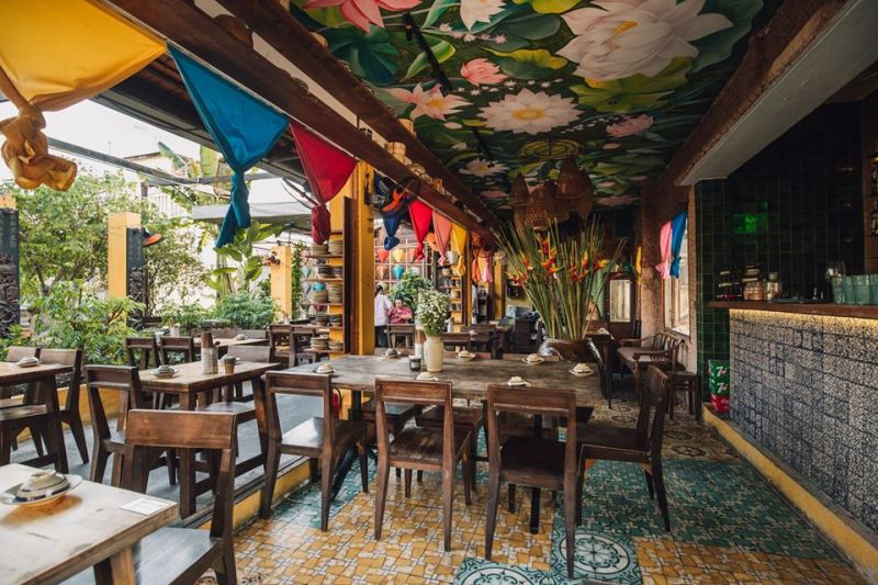 Không gian nhà hàng Secret Garden với bàn gỗ mộc, trần vẽ hoa sen và trang trí lồng đèn nhiều màu sắc.